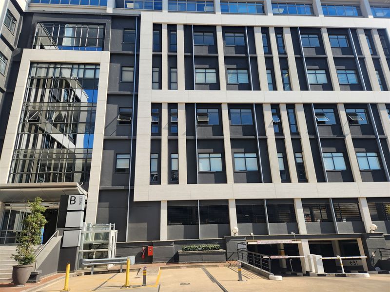 Modern multi-story office building facade featuring a contemporary glass and concrete design with a dedicated parking garage entrance and professional exterior finishes.