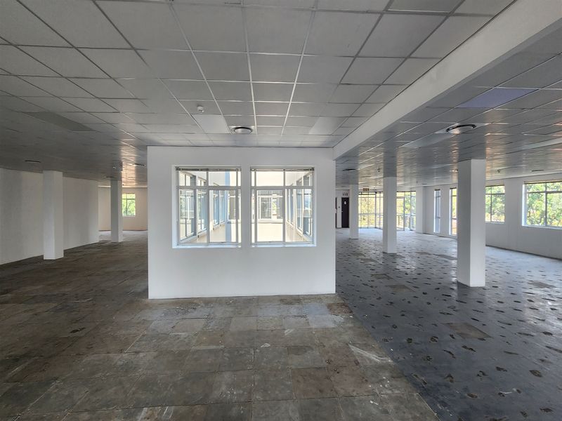 Spacious open-plan office area featuring a suspended ceiling, structural columns, and large windows providing ample natural light, currently awaiting floor refurbishment.