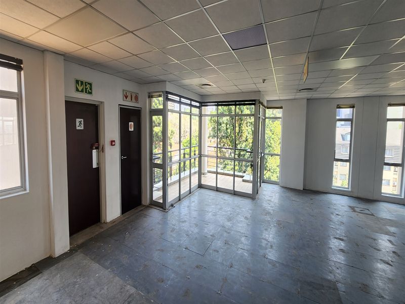 An empty office space featuring a suspended ceiling, large windows, and direct access to a small balcony area.