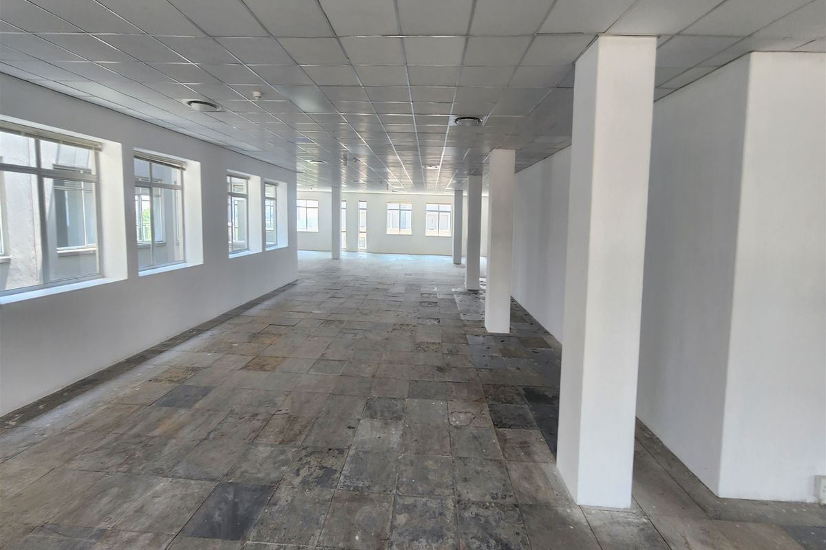 A spacious, vacant open-plan office area featuring structural columns, a suspended ceiling, and large windows providing ample natural light.