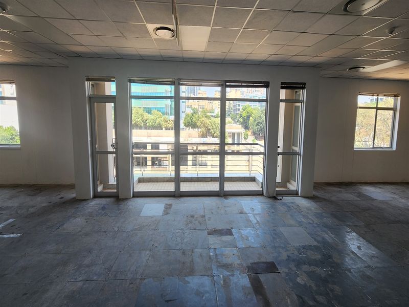 An empty office space featuring a suspended ceiling, large windows providing natural light, and direct access to a small balcony.