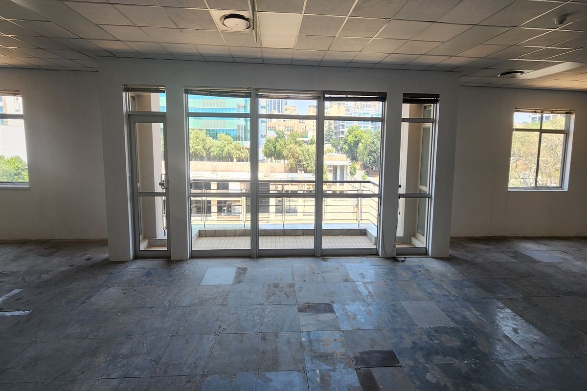 An empty office space featuring a suspended ceiling, large windows providing natural light, and direct access to a small balcony.
