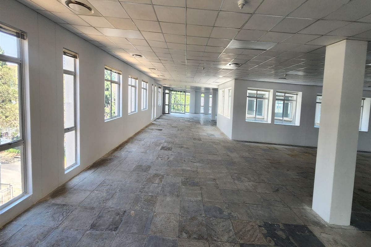 A spacious, open-plan office area featuring large windows, a suspended ceiling, and worn stone tile flooring, offering a blank canvas for customization.