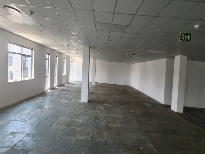 An empty, open-plan office space featuring a suspended ceiling, structural columns, and large windows providing natural light, ready for custom fit-out.