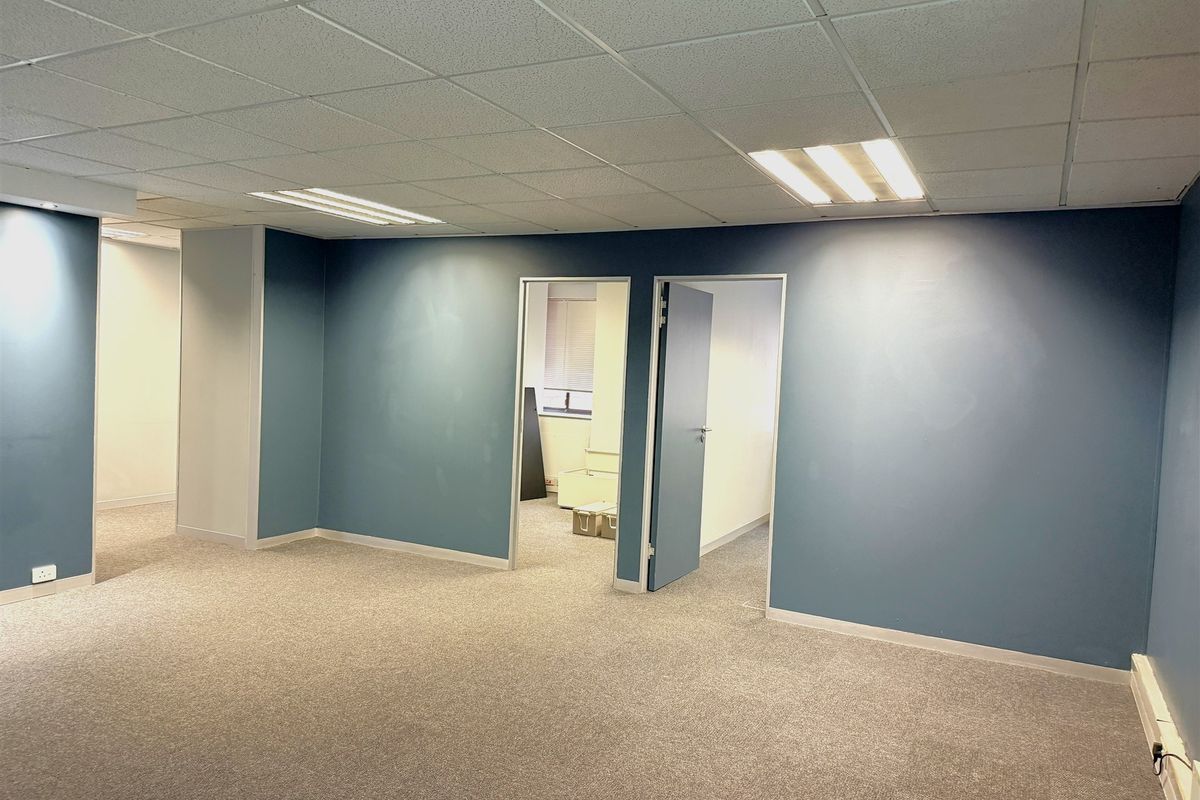 An empty office space featuring a suspended ceiling, recessed lighting, and carpeted flooring, with blue painted walls and internal access doors.