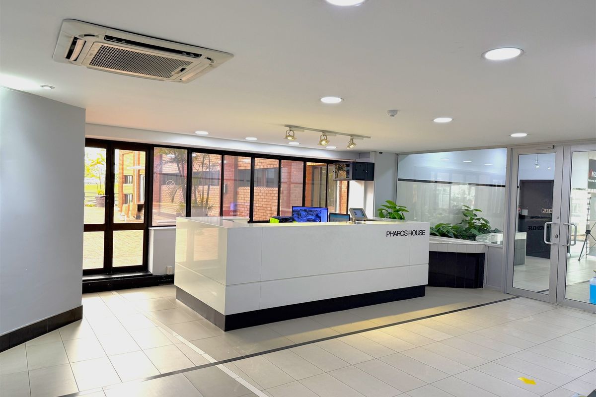 Modern office reception area featuring a sleek white reception desk, recessed ceiling lighting, cassette air conditioning, and large glass partitions.