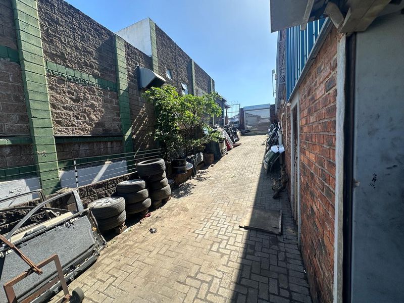 A narrow exterior side passage featuring brick paving, enclosed by perimeter walls with electric fencing and a metal gate at the rear.