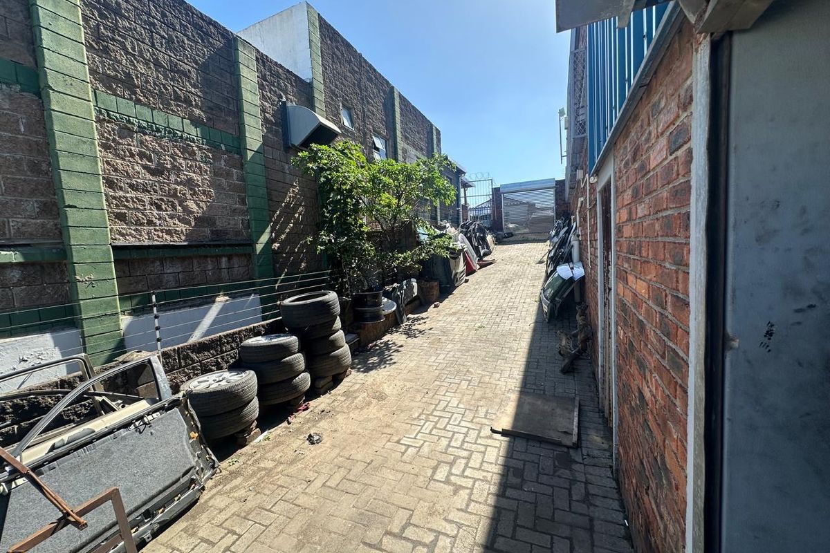 A narrow exterior side passage featuring brick paving, enclosed by perimeter walls with electric fencing and a metal gate at the rear.