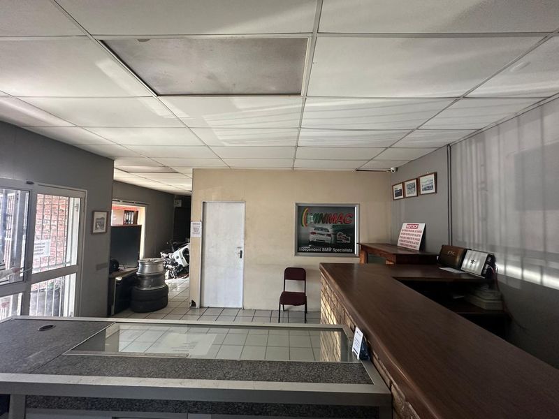 Commercial reception area featuring a built-in counter, tiled flooring, and a suspended ceiling, currently serving as an automotive service office.
