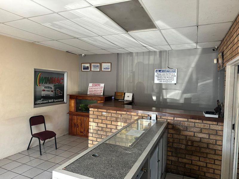 Commercial reception area featuring a brick-fronted service counter, tiled flooring, and a drop ceiling in a functional, dated office setting.