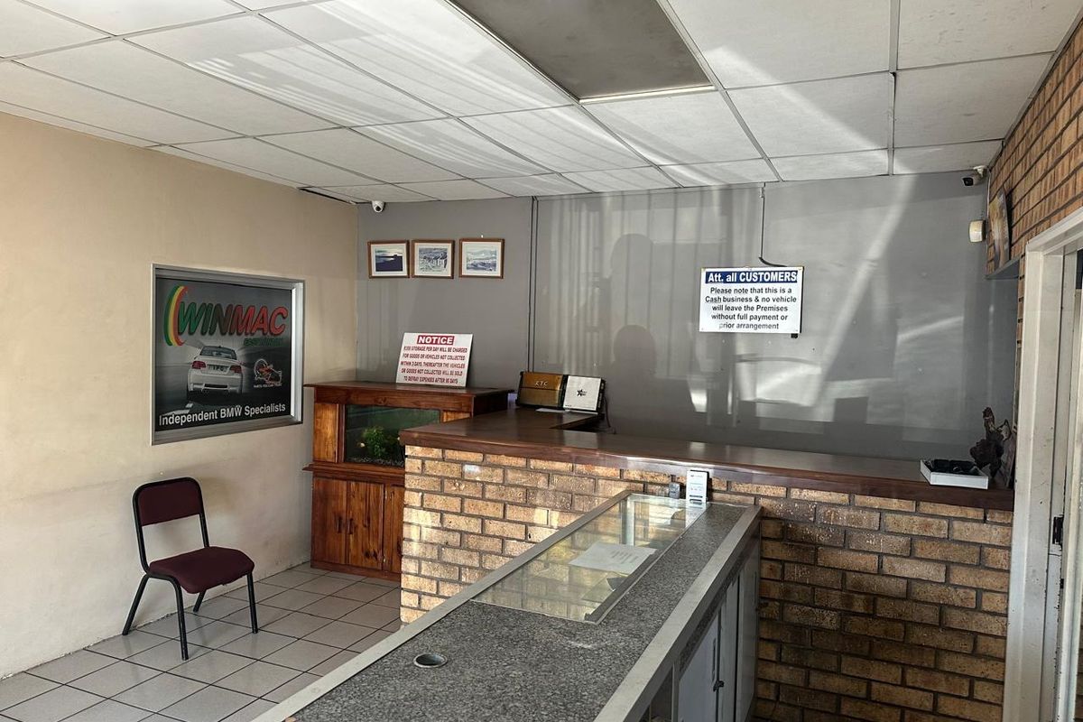 Commercial reception area featuring a brick-fronted service counter, tiled flooring, and a drop ceiling in a functional, dated office setting.