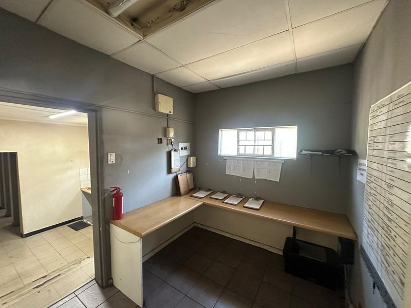 Functional office space featuring a built-in desk, suspended ceiling, and security window bars, suitable for administrative or commercial use.
