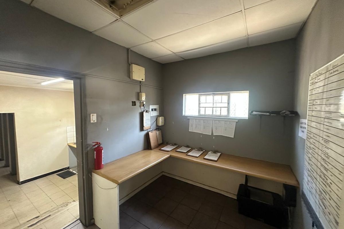 Functional office space featuring a built-in desk, suspended ceiling, and security window bars, suitable for administrative or commercial use.