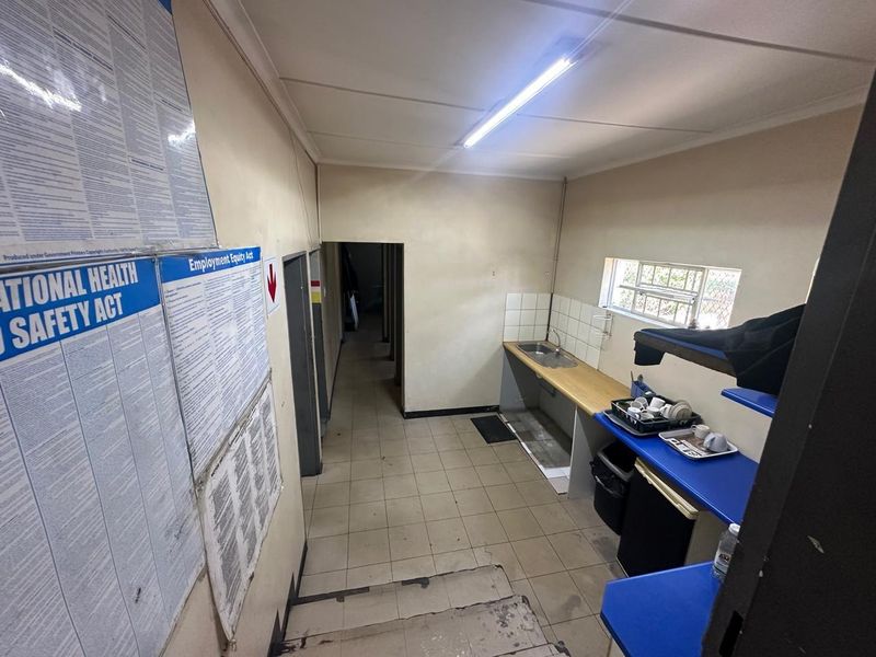 A functional commercial kitchenette area featuring a stainless steel sink, tiled flooring, and basic counter space, suitable for staff utility use.