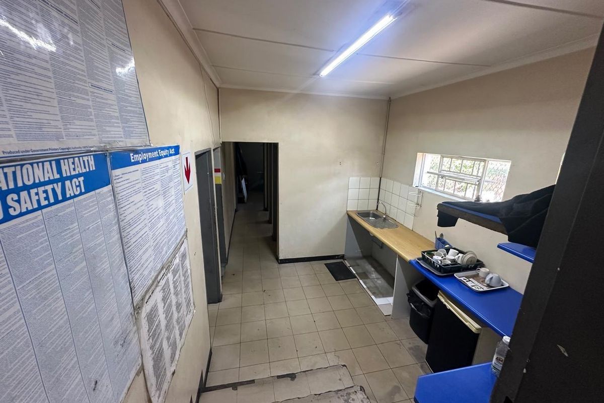A functional commercial kitchenette area featuring a stainless steel sink, tiled flooring, and basic counter space, suitable for staff utility use.