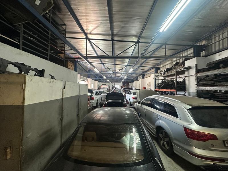 Spacious industrial garage facility featuring high exposed steel roof trusses, fluorescent lighting, and extensive built-in metal shelving for storage.