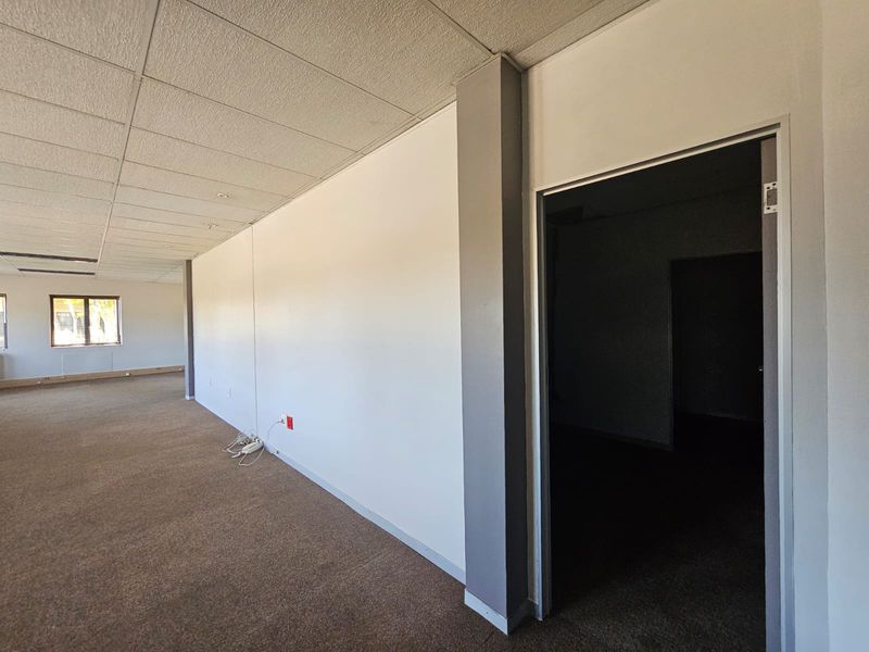 An empty office space featuring a suspended ceiling, carpeted flooring, and a neutral color palette, suitable for a professional workspace.
