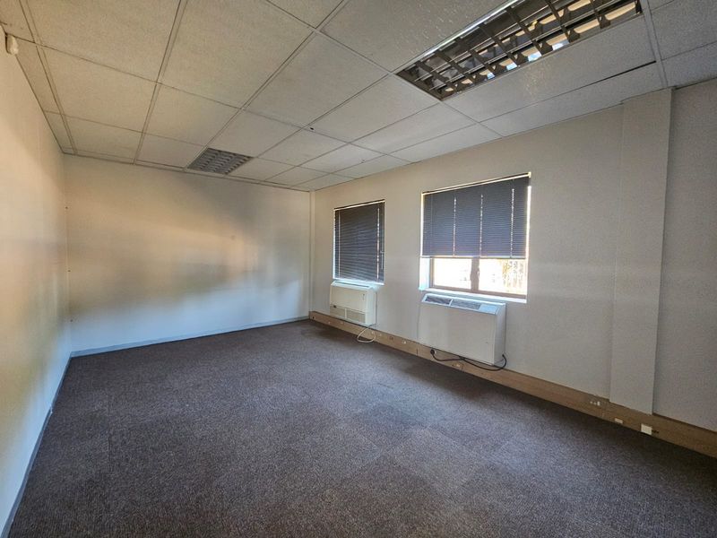 An empty office space featuring a suspended ceiling, recessed lighting, wall-mounted air conditioning units, and carpeted flooring.
