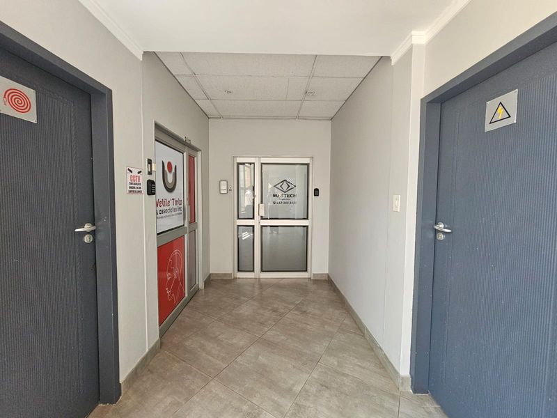 A clean, well-maintained commercial hallway featuring tiled flooring, a drop ceiling with recessed lighting, and multiple secure access-controlled office entry doors.