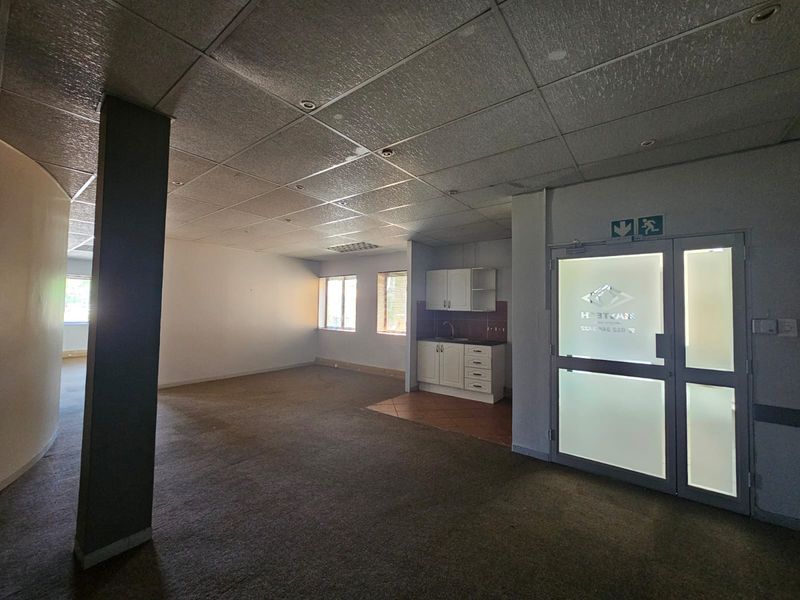 Open-plan office space featuring a kitchenette, suspended ceiling, recessed lighting, and a glass entrance door, suitable for a professional business environment.