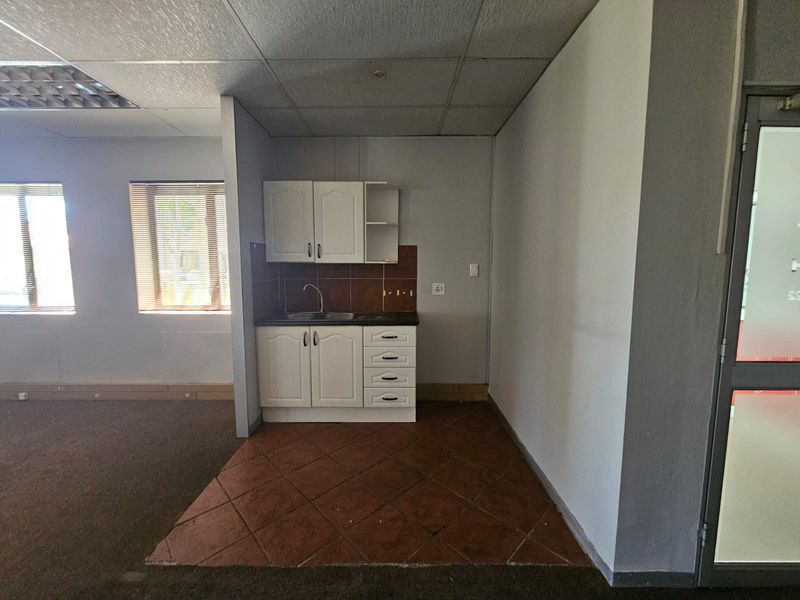A compact kitchenette area featuring built-in cabinetry, a sink, and tiled flooring, situated within an open-plan office space.