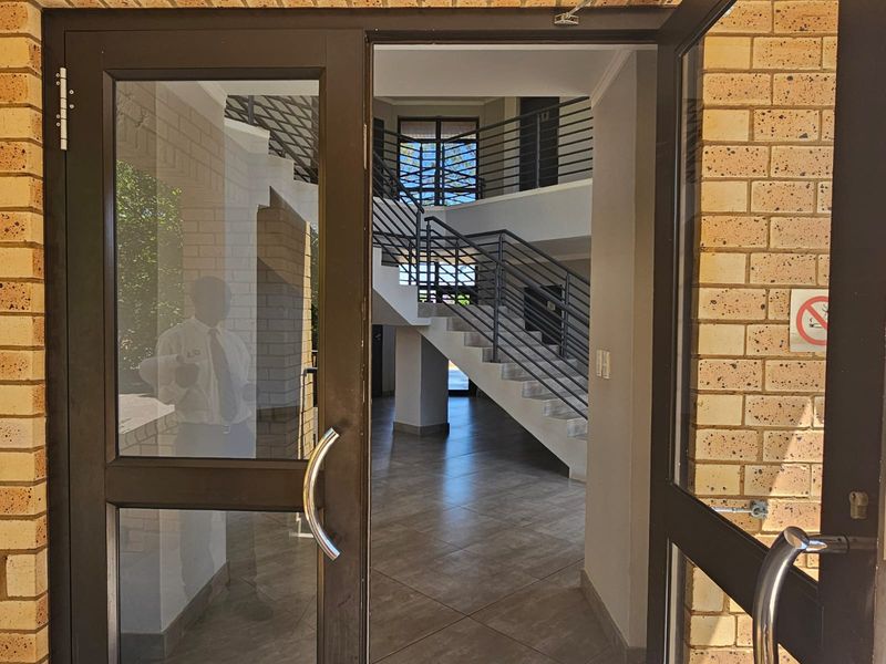 Entrance area featuring glass-panelled doors, tiled flooring, and a central staircase with metal balustrades leading to upper levels.