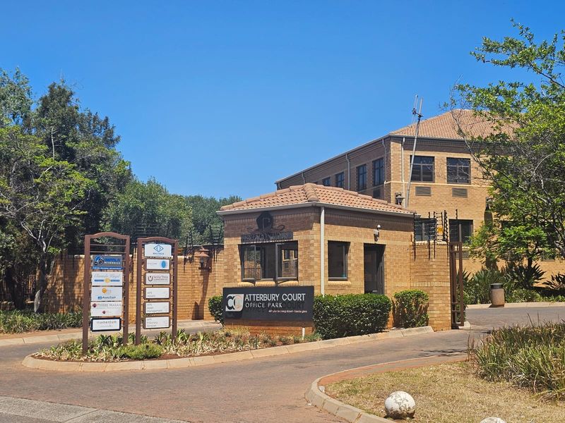 Front entrance view of Atterbury Court Office Park featuring a brick security guard house, paved driveway, and professional business signage.