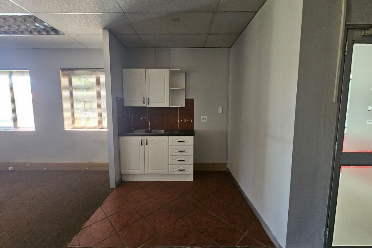 A compact kitchenette area featuring built-in cabinetry, a sink, and tiled flooring, situated within an open-plan office space.