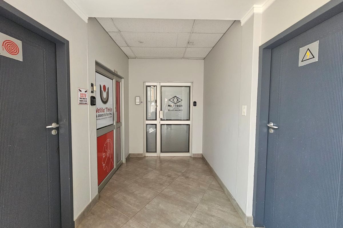 A clean, well-maintained commercial hallway featuring tiled flooring, a drop ceiling with recessed lighting, and multiple secure access-controlled office entry doors.
