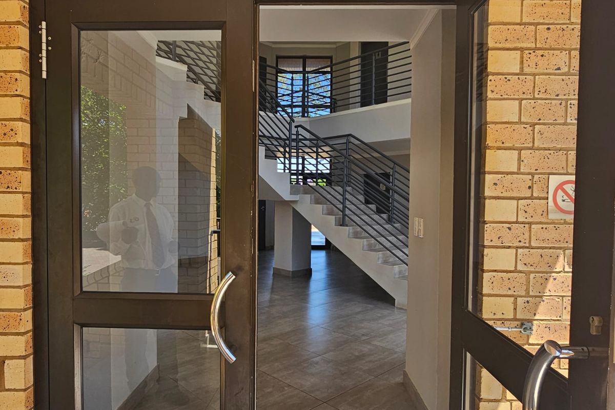 Entrance area featuring glass-panelled doors, tiled flooring, and a central staircase with metal balustrades leading to upper levels.