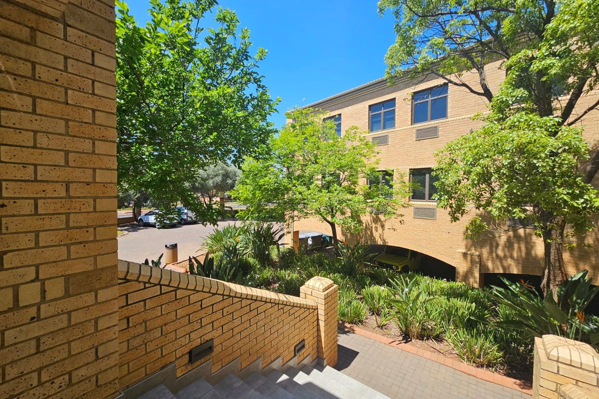 Exterior view of a multi-story face brick commercial building featuring a paved staircase, landscaped garden area, and integrated undercover parking.