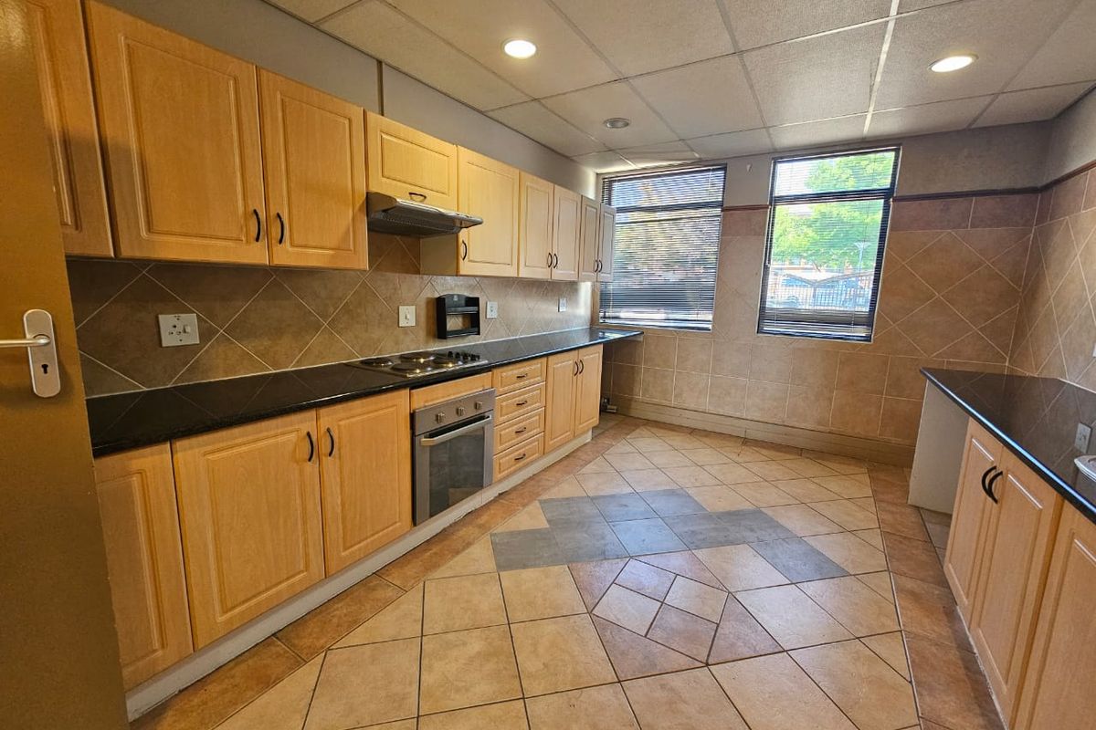 A functional kitchen featuring light wood cabinetry, dark laminate countertops, integrated oven and hob, tiled backsplash, and tiled flooring with recessed lighting.