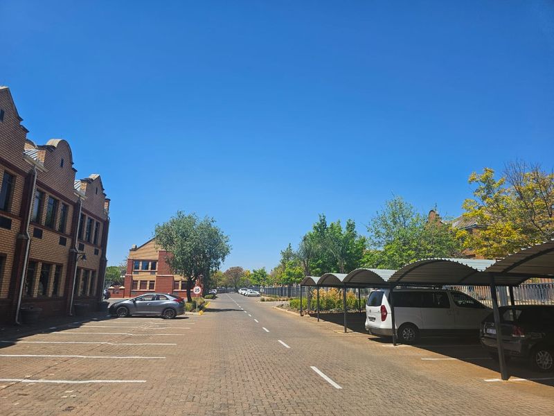 Exterior view of a business property featuring a paved driveway, marked parking bays, and covered parking structures alongside brick office buildings.
