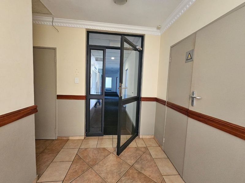 A functional commercial hallway featuring tiled flooring, dado rails, and a glass-panelled entrance door leading to an internal corridor.
