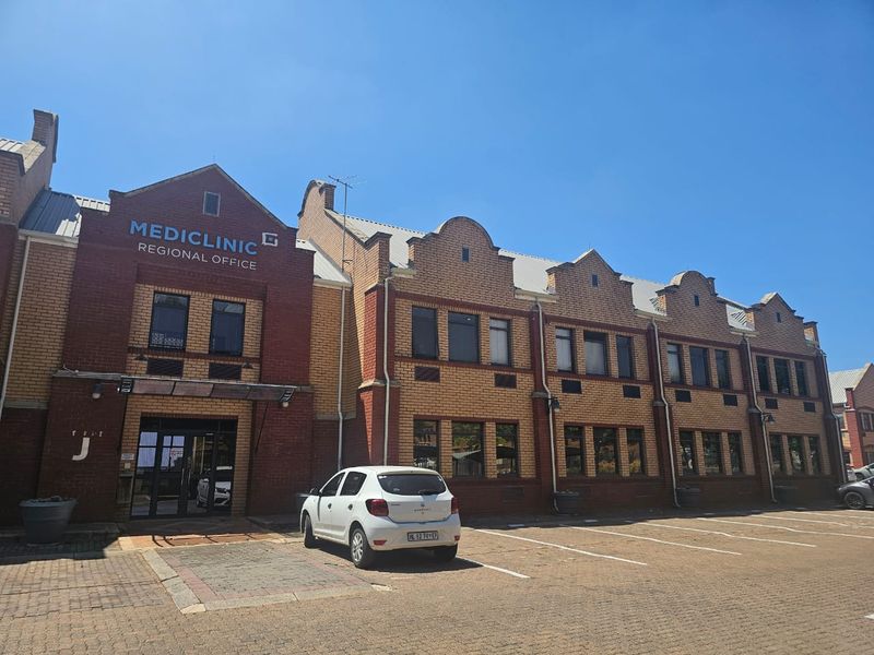 Front elevation of a multi-story brick commercial office building featuring gabled roof lines, large windows, and an adjacent paved parking area.