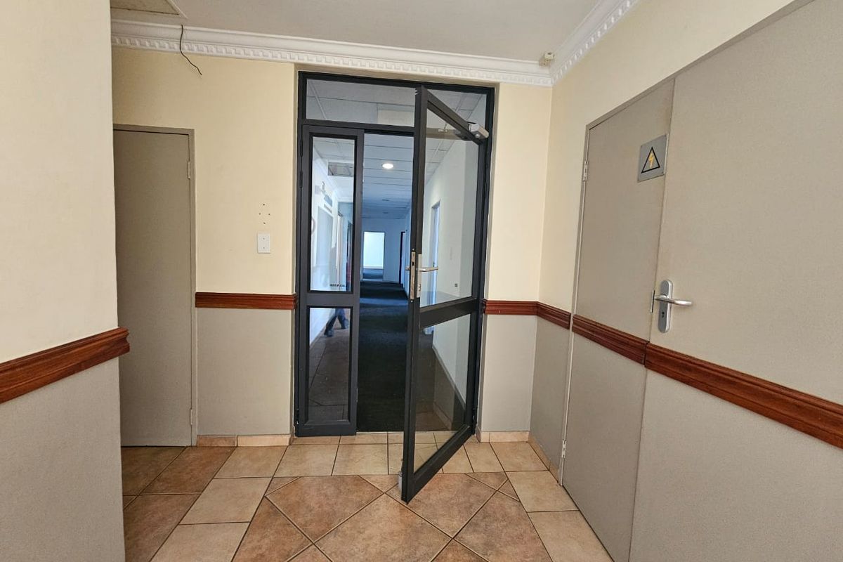 A functional commercial hallway featuring tiled flooring, dado rails, and a glass-panelled entrance door leading to an internal corridor.