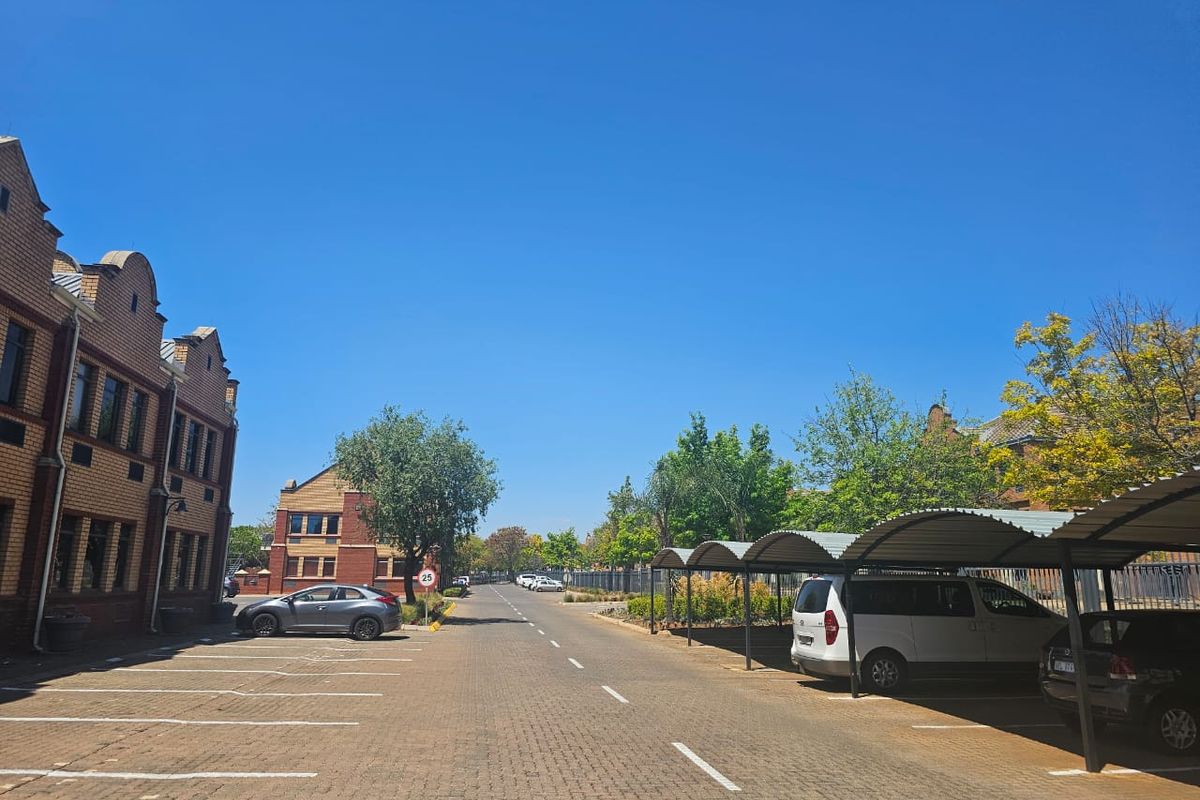 Exterior view of a business property featuring a paved driveway, marked parking bays, and covered parking structures alongside brick office buildings.
