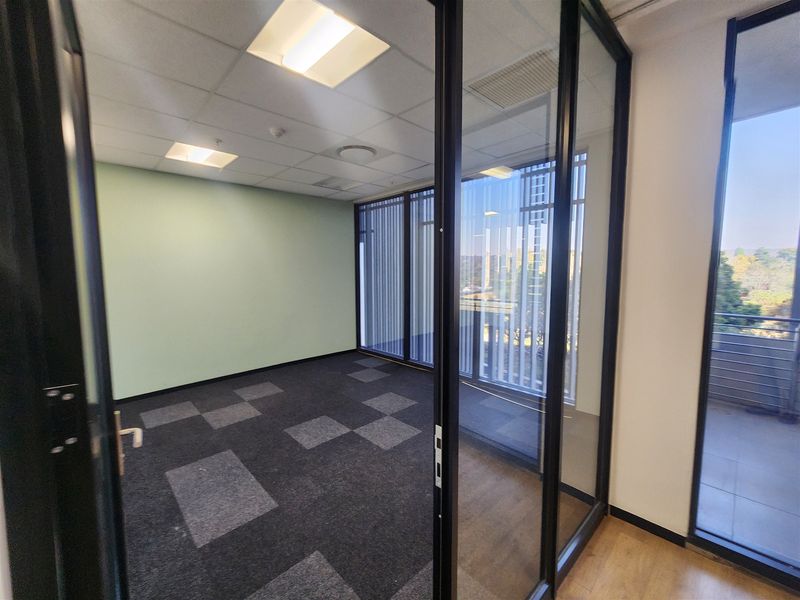 A bright, empty office space featuring modern glass partitioning, carpet tiles, and a suspended ceiling with recessed lighting, offering a professional work environment.