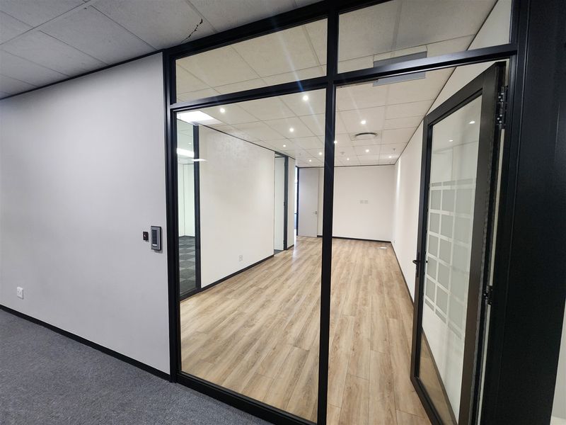 A modern, vacant office space featuring glass partitioning, wood-look flooring, and recessed lighting, offering a clean and professional environment.
