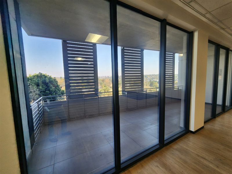 A modern office balcony featuring tiled flooring, stainless steel balustrades, and slatted privacy screens, offering an elevated view.