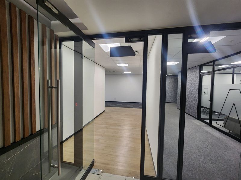 Modern vacant office space featuring glass partitions, suspended ceilings, and a mix of wood-look vinyl and carpet flooring, offering a professional and clean aesthetic.