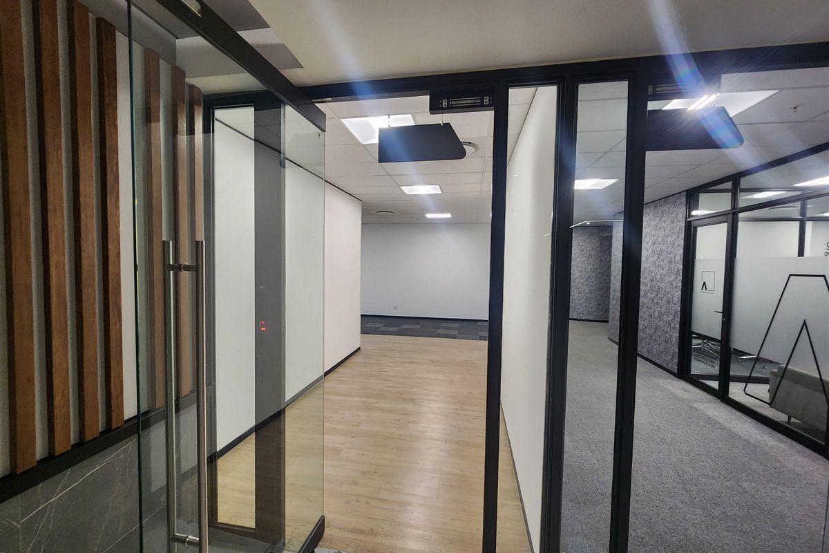 Modern vacant office space featuring glass partitions, suspended ceilings, and a mix of wood-look vinyl and carpet flooring, offering a professional and clean aesthetic.