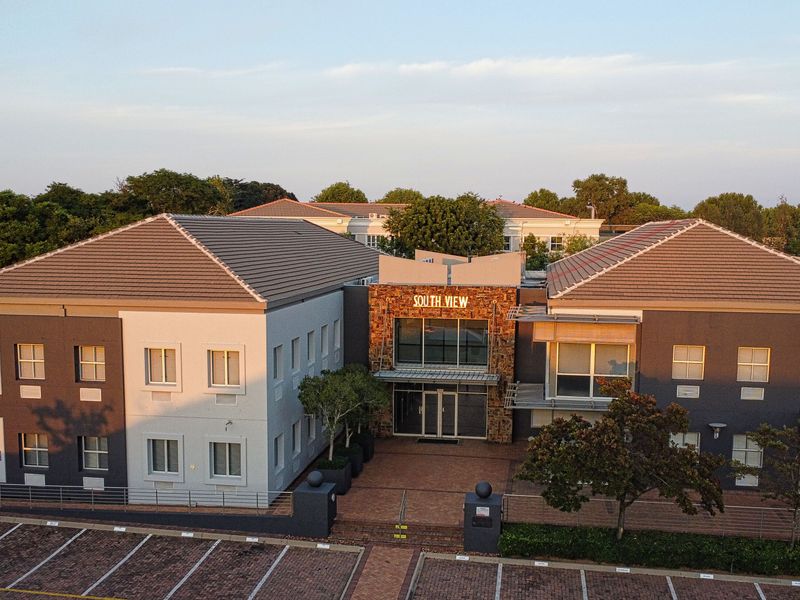 Aerial view of the South View office complex, featuring a modern facade with stone cladding, tiled roofing, and an extensive paved parking area.