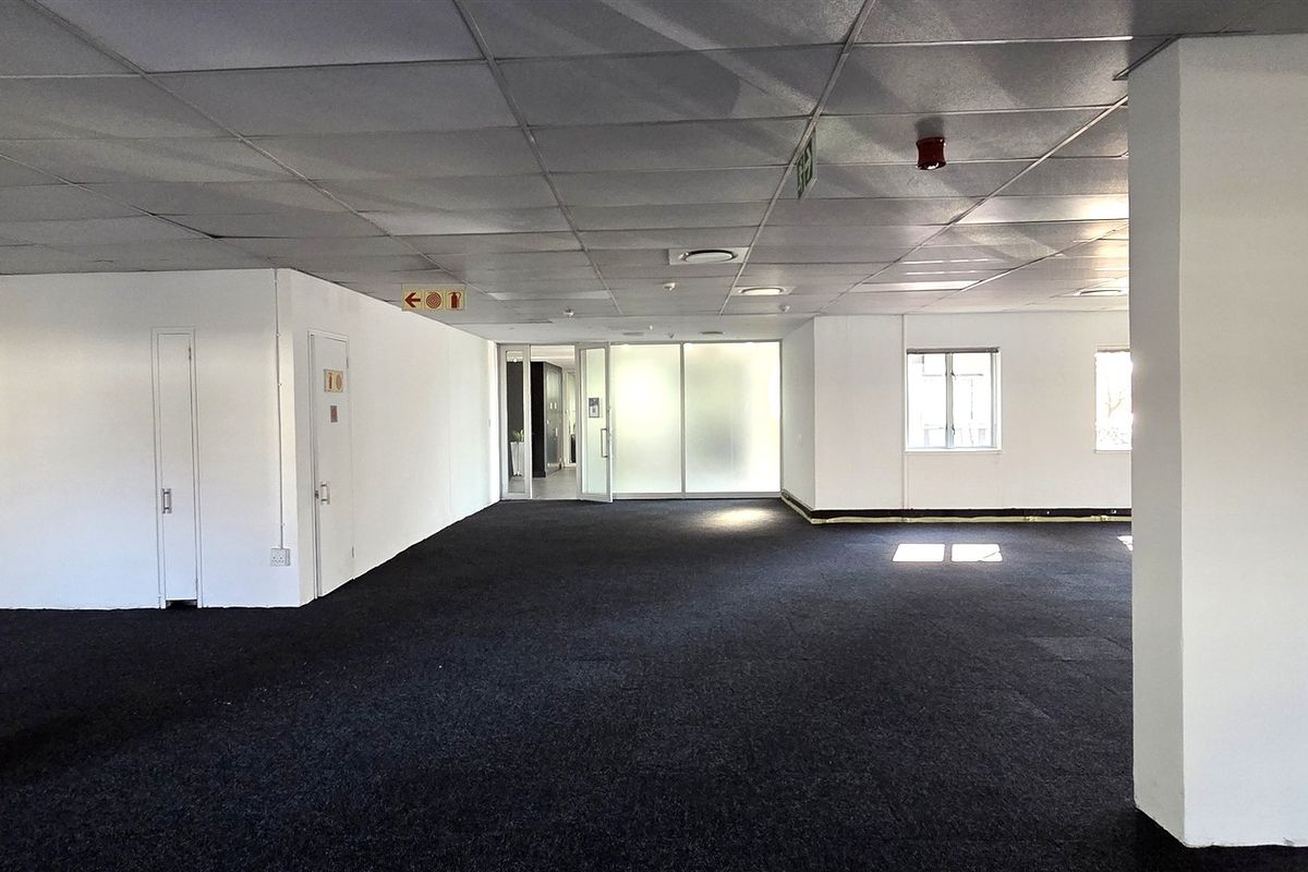 Spacious open-plan office area featuring a suspended ceiling, structural columns, and dark carpeting, offering a versatile workspace with natural light.