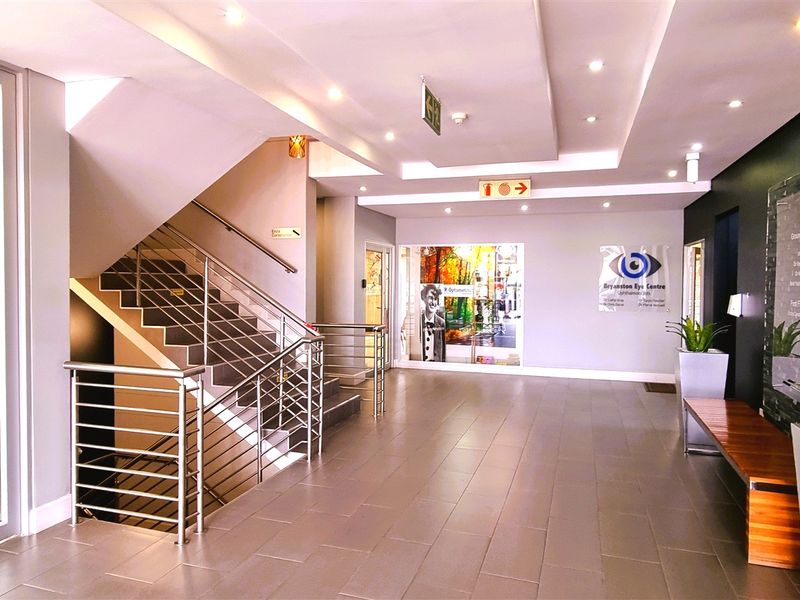 Modern office building entrance lobby featuring tiled flooring, a prominent staircase with stainless steel balustrades, and recessed ceiling lighting.