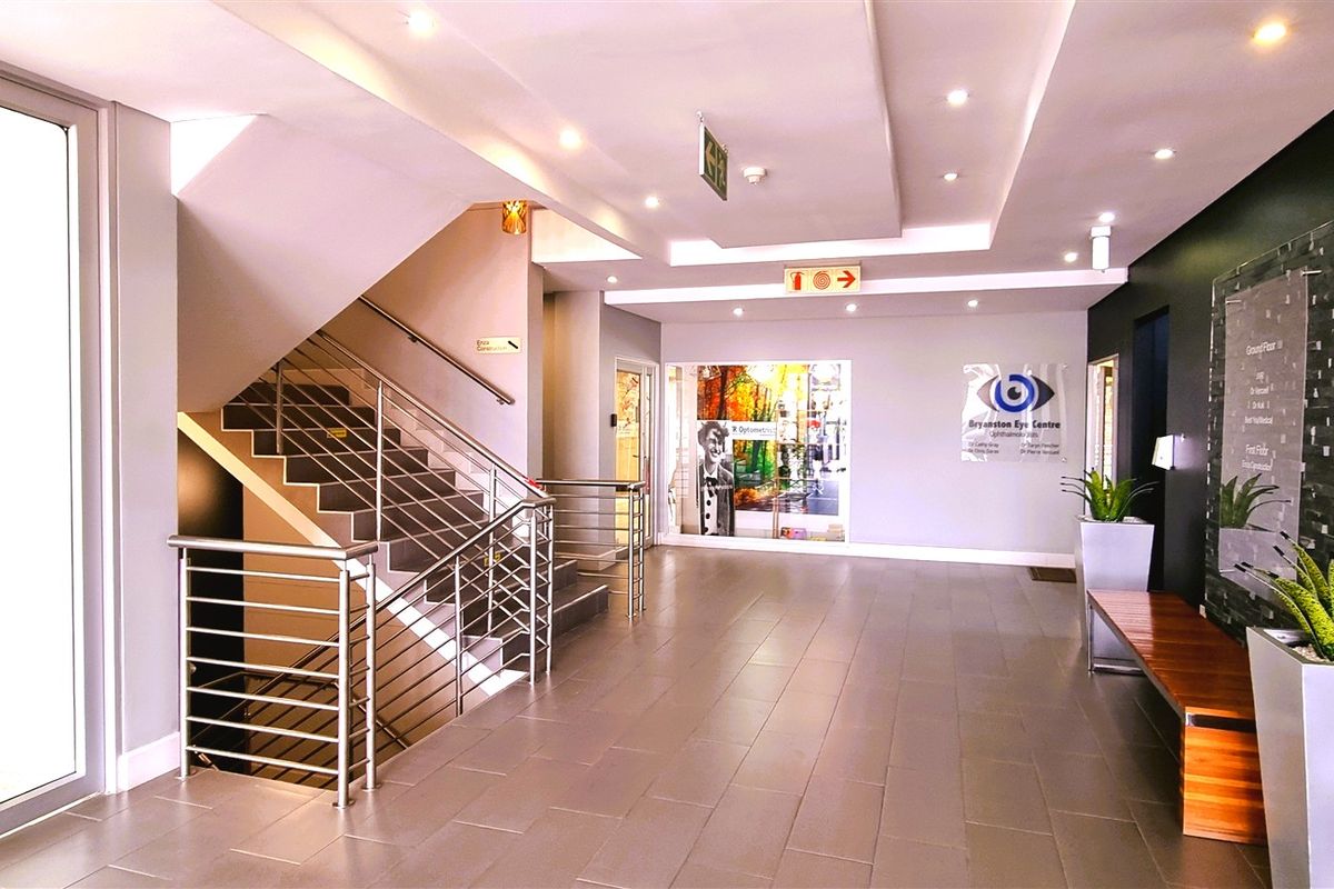 Modern office building entrance lobby featuring tiled flooring, a prominent staircase with stainless steel balustrades, and recessed ceiling lighting.