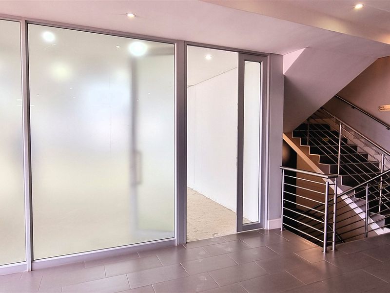 Modern office building entrance lobby featuring frosted glass partitions, tiled flooring, and a staircase with stainless steel railings.