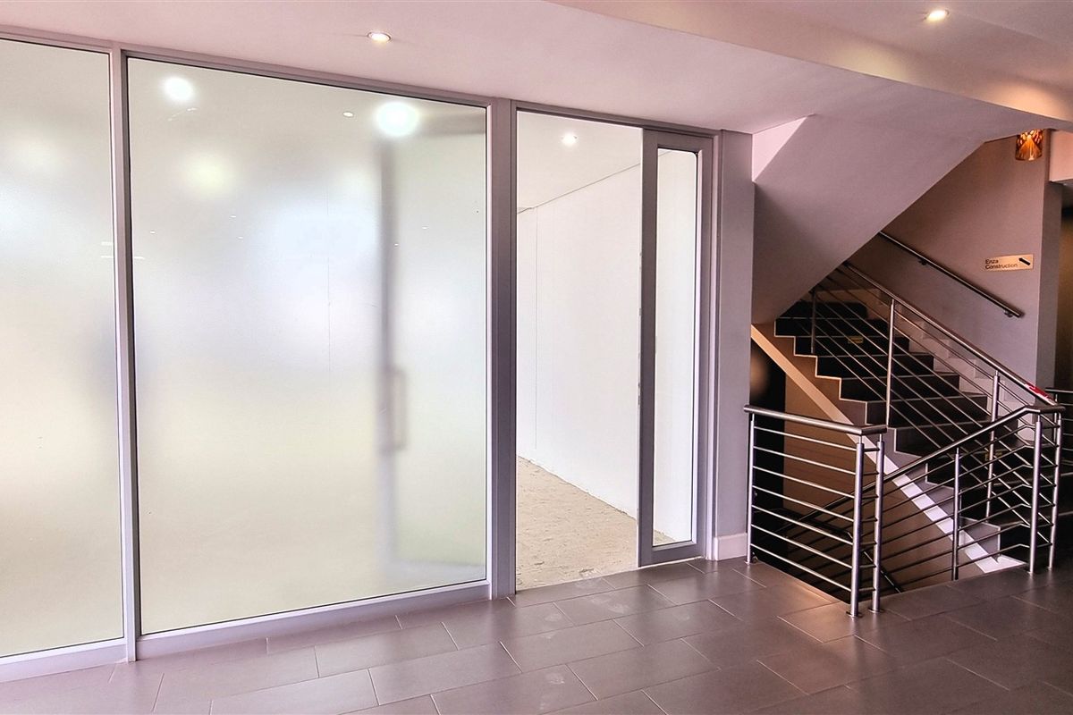 Modern office building entrance lobby featuring frosted glass partitions, tiled flooring, and a staircase with stainless steel railings.