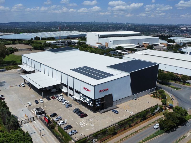 Aerial view of a large industrial warehouse facility featuring solar panels, dedicated loading bays, and an extensive paved parking area.