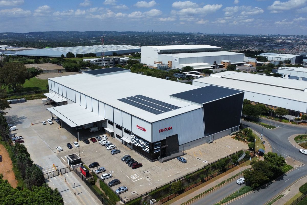 Aerial view of a large industrial warehouse facility featuring solar panels, dedicated loading bays, and an extensive paved parking area.